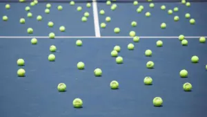 Many yellow tennis balls scattered across a blue hard court tennis surface.