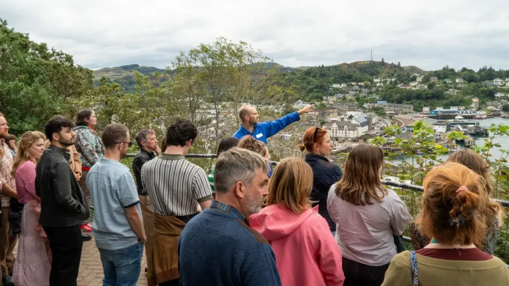 A tour guide points towards a coastal town for a group of diverse tourists.