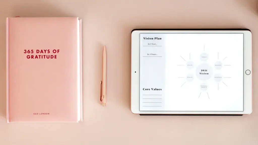 A soft pink planner and tablet displayed on a clean white minimalist desk surface.