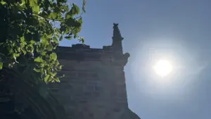A stone church tower peak silhouetted against a bright sun in a clear sky.