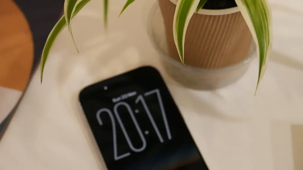 Smartphone resting on a table beside a plant, showing time displayed on screen.
