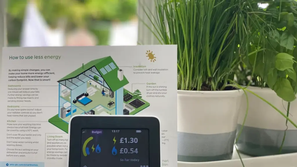 Smart energy monitor displaying costs on a kitchen windowsill with green plants.
