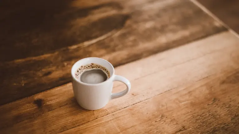 White ceramic coffee mug resting on a wooden table in the UK.