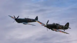Classic Spitfire and Hurricane fighter planes flying in formation during a historic air show.