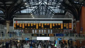 Busy London train station concourse featuring a large digital departure information board.