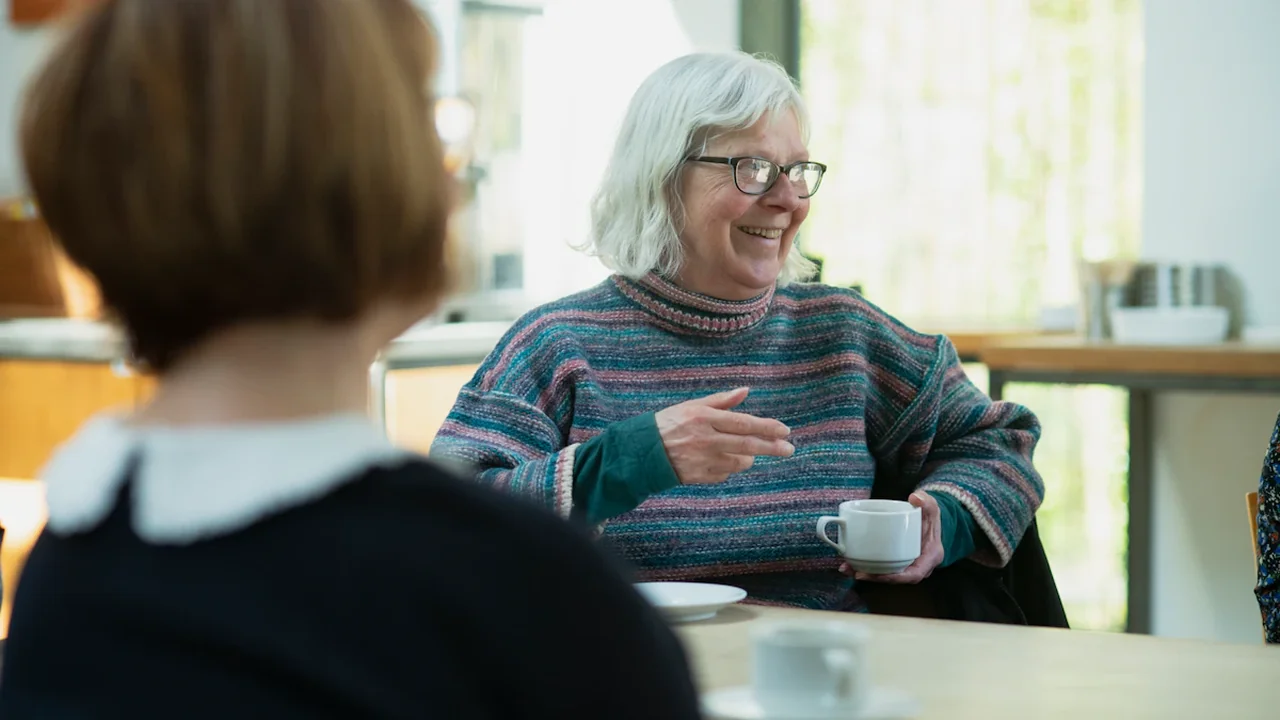 Two women engaged in a gentle, warm conversation over coffee at a table.