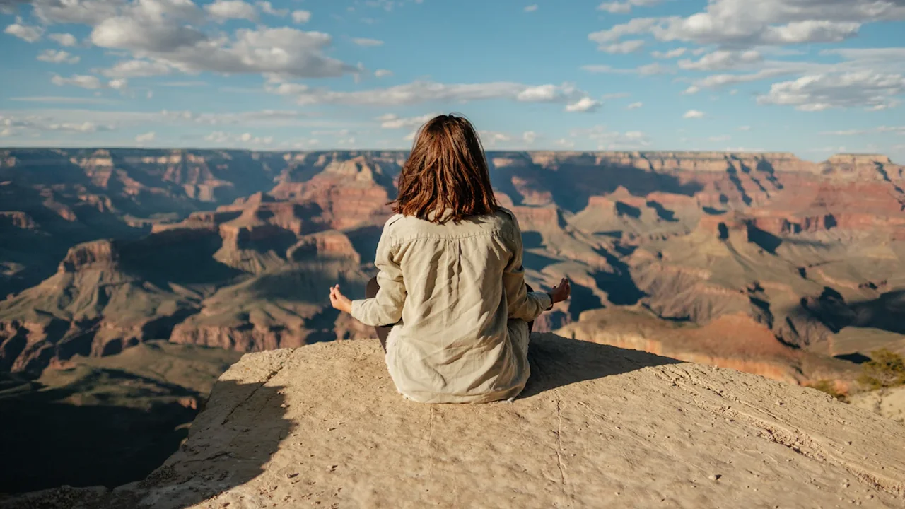Person sits in peaceful meditation overlooking the vast and dramatic landscape of the Grand Canyon.